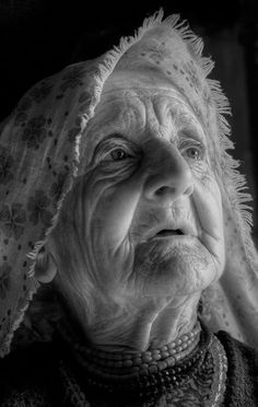 an old woman wearing a headdress and looking into the distance with her eyes wide open