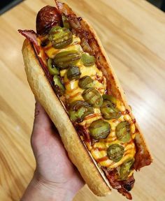 a person holding a hot dog with toppings on it in front of a wooden table