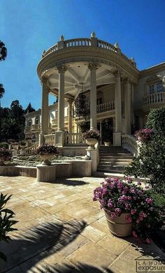 a gazebo in the middle of a garden with pink flowers and trees around it