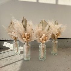 three glass vases with dried flowers in them