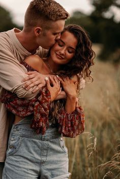 a man and woman embracing each other in the middle of a field with tall grass