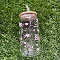 a hello kitty tumbler with pink hearts on it is sitting in the green grass