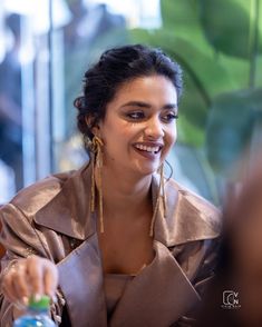 a woman sitting at a table smiling and holding a bottle