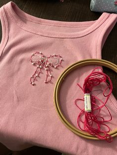 a pink shirt with a bow on it next to some yarn and a wooden hoop