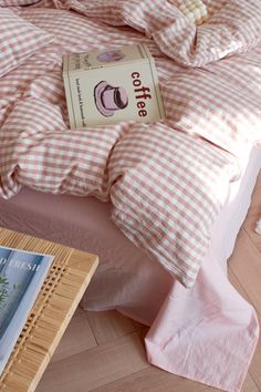 a bed with pink gingham comforter and pillows on it next to a book