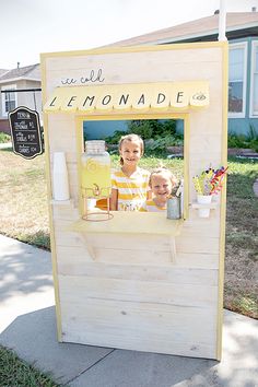 two children are sitting in a lemonade kiosk on the side of the road