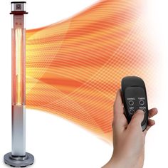 a hand holding a remote control next to an electric heater and thermometer