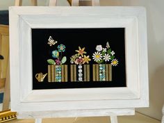 a white frame with some flowers and other things in it on top of a table