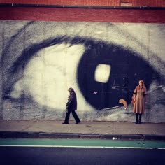 two people walking past a wall with an eye painted on it