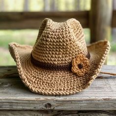 a straw hat with a brown flower on it sitting on top of a wooden bench