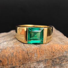 a gold ring with an emerald colored stone on top of a piece of drift wood