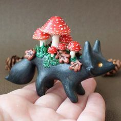 a hand holding a tiny figurine with mushrooms on it's back and an animal in the foreground