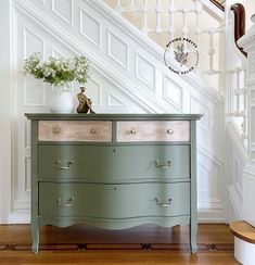 an old dresser painted green and white with flowers on top in front of the stairs