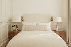 a bed with white linens and pillows in a bedroom next to two lamps on either side of the bed