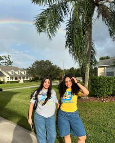 two young women standing next to each other in front of a tree with a rainbow in the background