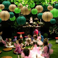 a group of children sitting on the grass in front of paper lanterns and fairy decorations