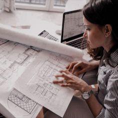 a woman sitting at a desk looking at blueprints