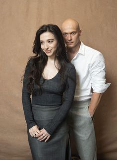 two people standing next to each other in front of a brown background