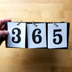 a person holding up three numbered cards with the numbers 665 and 536 on them