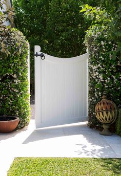 an open white gate in the middle of a garden