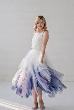 a woman in a white dress with blue and purple layers on her skirt is posing for the camera