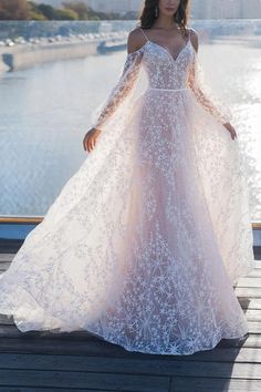 a woman in a long white dress standing on a dock with her arms around her waist