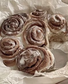 several cinnamon rolls sitting on top of wax paper in a bowl with a spoon next to it