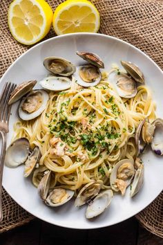 a plate of pasta with clams and parsley on the side next to lemon wedges