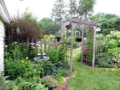 a garden filled with lots of plants and flowers next to a wooden arbor covered in hanging pots