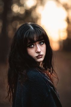 a woman with black hair and blue eyes is standing in front of the sun shining through trees