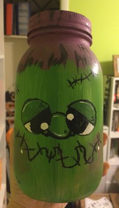 a person holding up a painted jar with an image of a green monster on it