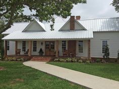 a white house with a metal roof in the country side yard and walkway leading to it