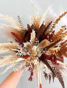 a hand holding a bouquet with dried flowers and feathers on it's centerpiece