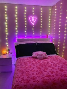 a pink bed in a room with lights on the wall and a teddy bear laying on it