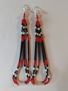 three pairs of black and red beaded earrings hanging from hooks on a white surface