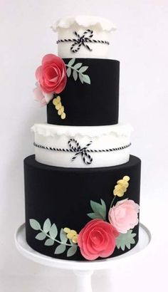 a three tiered cake decorated with flowers and ribbons on a white stand against a white wall