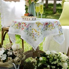 a table with flowers and two glasses of wine on it, sitting in the grass