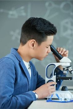 a young man looking through a microscope at something in front of him on a table