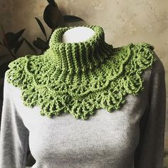 a woman wearing a green crocheted neck scarf on top of a mannequin