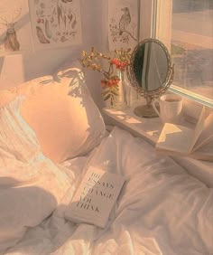 a bed with white sheets, pillows and a book on top of it next to a window