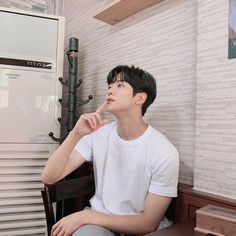 a young man sitting on top of a wooden table next to a white refrigerator freezer