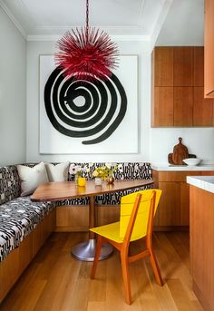 a dining room table with yellow chairs next to a bench and artwork on the wall