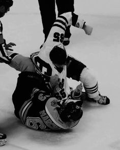 two hockey players collide on the ice as one falls to the ground in front of another player