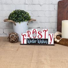 a wooden sign that says frosty water wishes next to a candle and potted plant