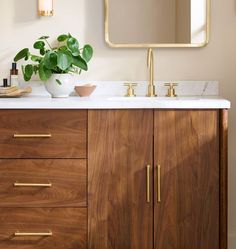 a bathroom vanity with marble counter top and wooden cabinet, gold accents on the mirror