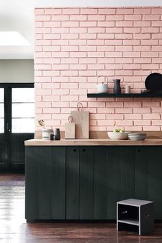 a pink brick wall in a kitchen with green cupboards and shelves on the side