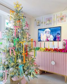 a brightly colored christmas tree in a living room with pink furniture and pictures on the wall