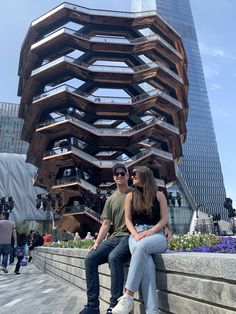 two people are sitting on a wall in front of a building with spiral staircases