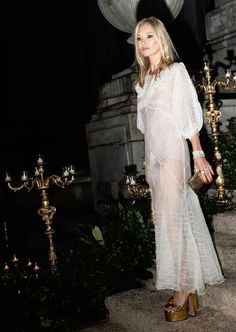 a woman in a sheer white dress standing next to candles