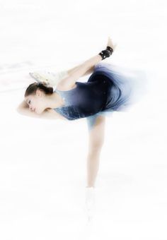 a female figure skating on the ice in a blue dress and black gloves with her arms outstretched